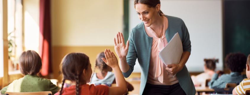 Lehrerin in eine Klasse, die mit einer Schülerin High Five gibt.