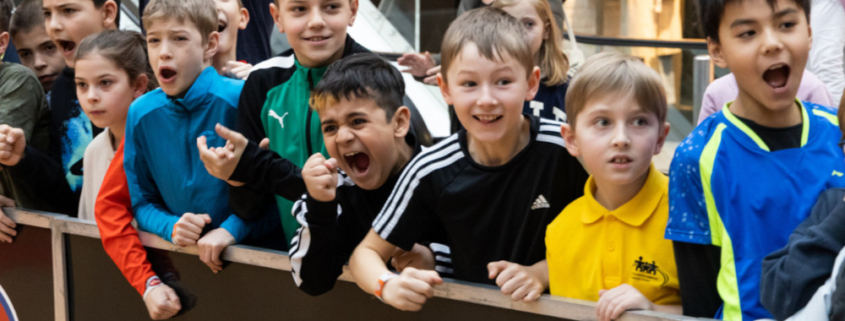 Eine Gruppe jubelnder und anfeuernder Kinder und der Text: Servus bewegt Kinder - Die bewegte Schule. motion4kids. Anmeldung ab Herbst.