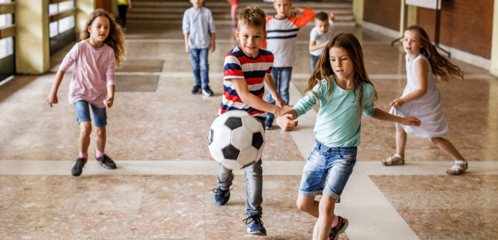 Eine Gruppe von Grundschulkindern hat Spaß beim Fußballspielen im Schulflur