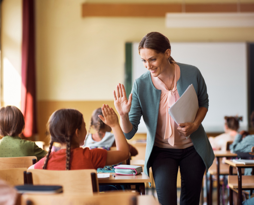 Lehrerin in eine Klasse, die mit einer Schülerin High Five gibt.