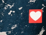 Ein weißes Herz in einem roten Quadrat aufgemalt auf einer fleckigen Wand.