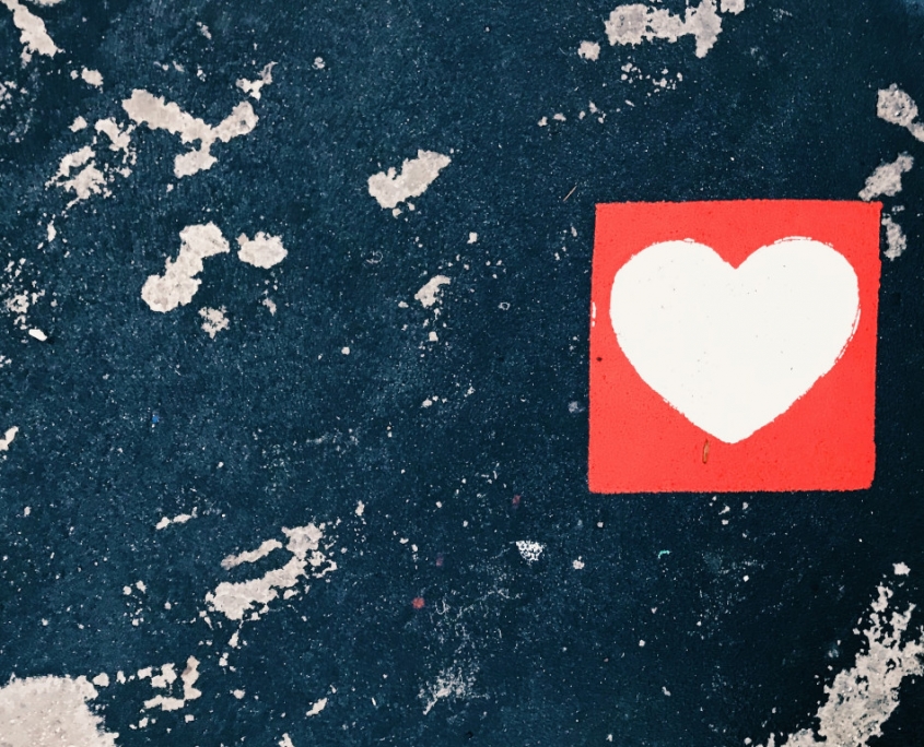 Ein weißes Herz in einem roten Quadrat aufgemalt auf einer fleckigen Wand.