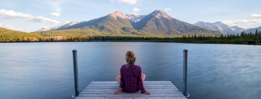 Eine Frau sitzt auf einem Steg und schaut hinaus auf den See