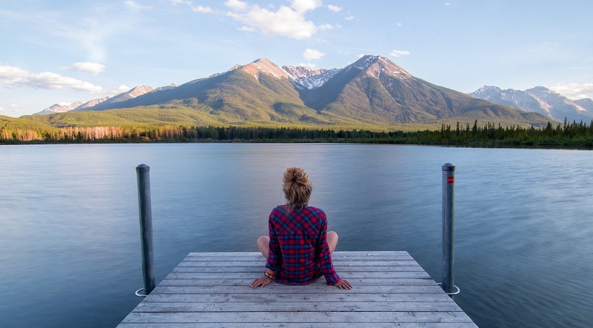 Eine Frau sitzt auf einem Steg und schaut hinaus auf den See