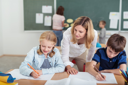 Lehrerin unterstützt im Unterricht eine Schülerin und einen Schüler