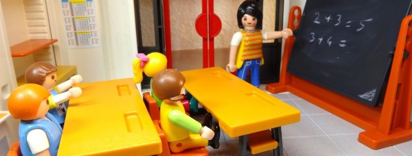 Ein Playmobil-Klassenzimmer mit Lehrerin an der Tafel und vier Schülerinnen und Schülern