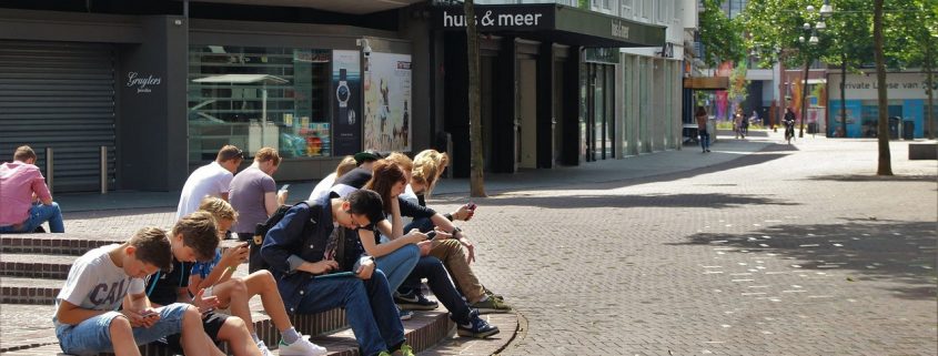 Kinder und Erwachsene sitzen auf einem öffentlichen Platz und starren in ihre Handys